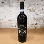 Botella de vino tinto Primitivo di Manduria Di Camillo junto a copa servida sobre fondo rústico italiano