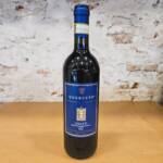 Botella de vino tinto Chianti DOCG Querceto junto a copa servida sobre fondo toscano rústico